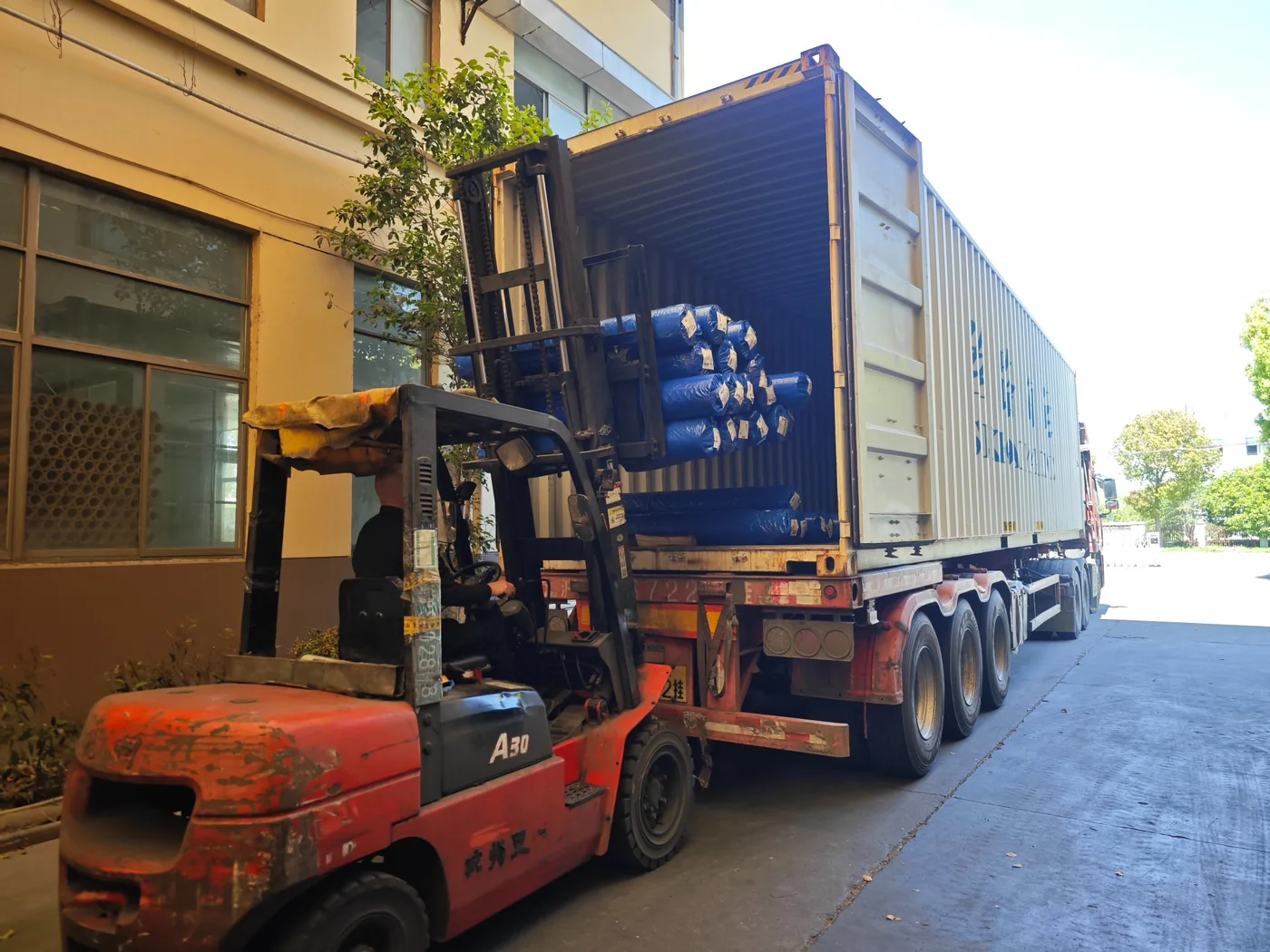 Forklift loading wrapped woven fabric rolls into a shipping container